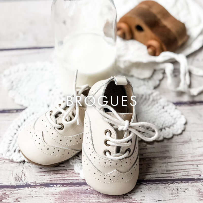 White brogue shoes on a wooden surface with a white rug and wooden object in the background.