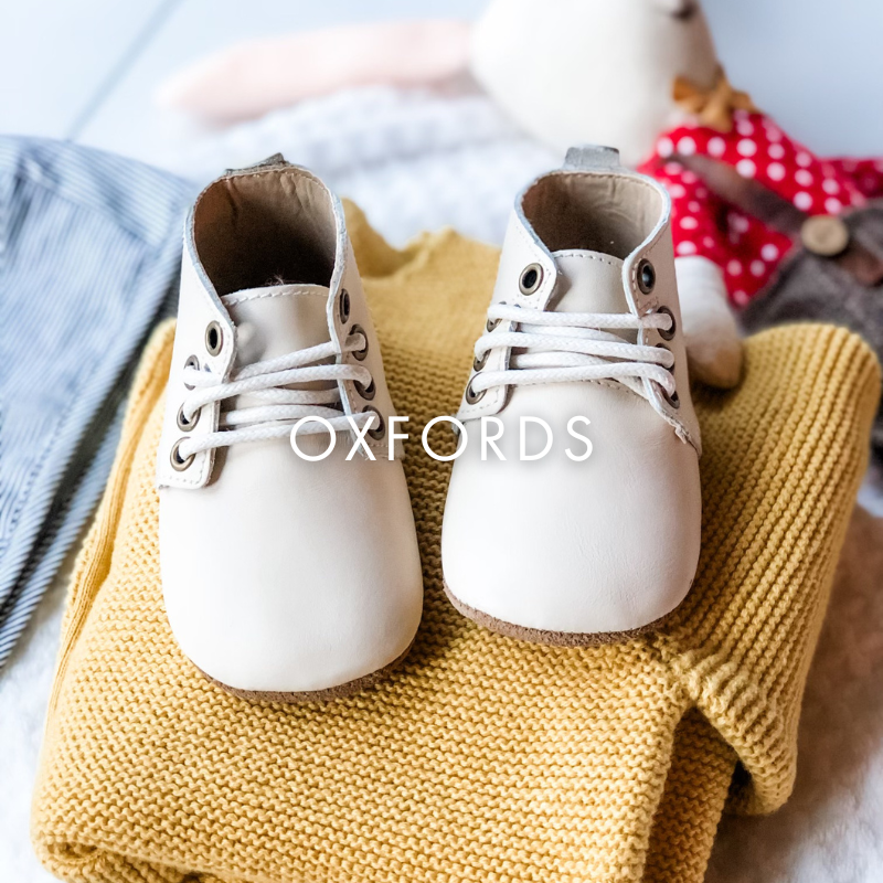 Pair of white oxford shoes on a yellow fabric with 'OXFORDS' text.