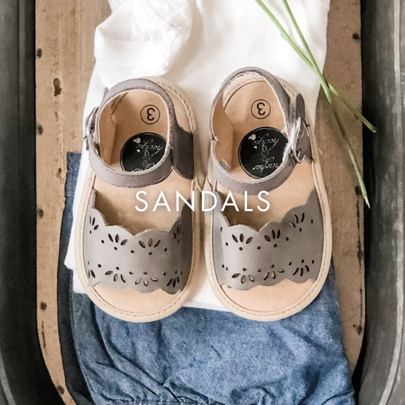 Pair of sandals with decorative cut-out design on a wooden surface.