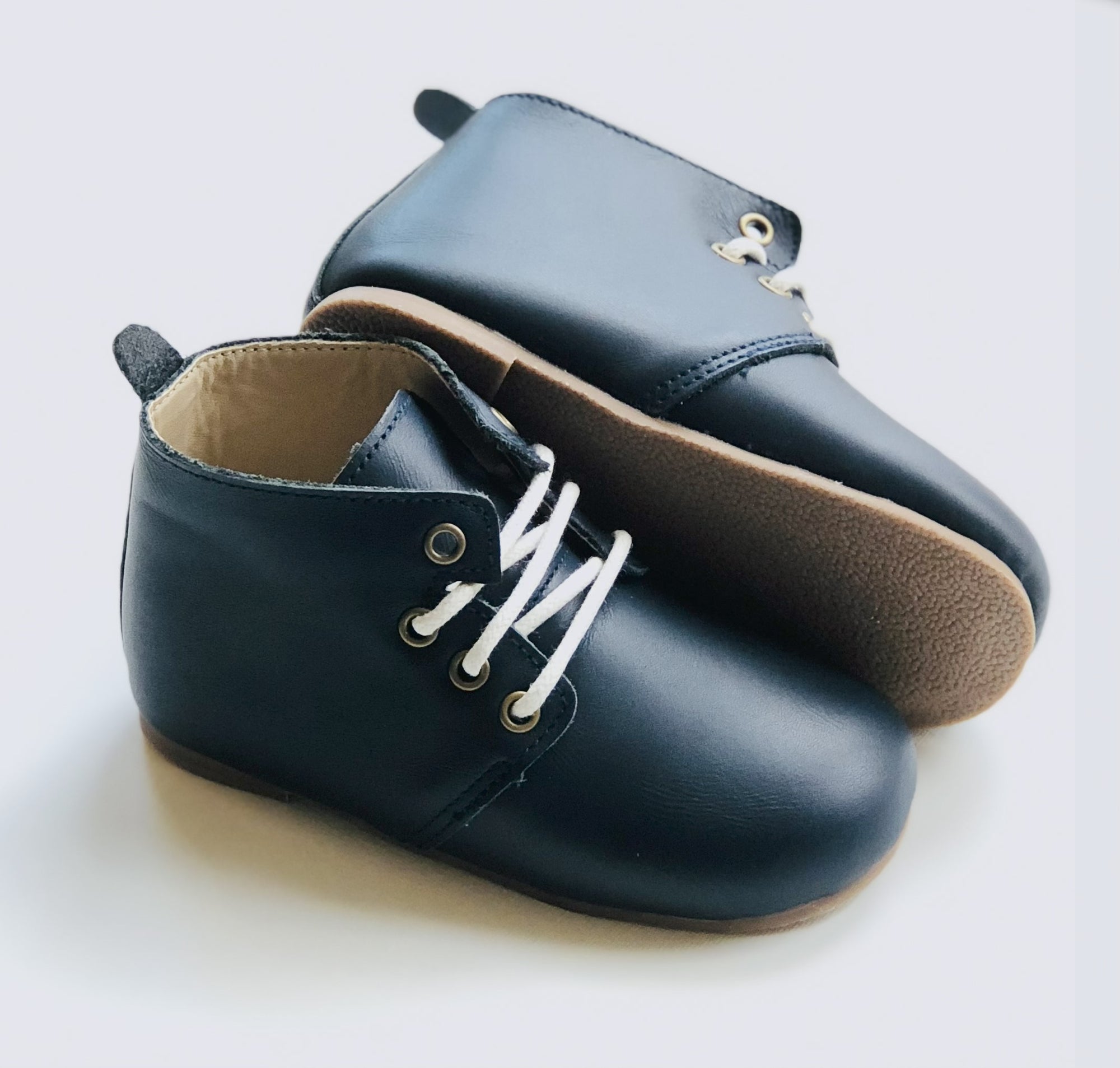 Dark navy leather baby Oxford shoes with white laces, tan soft soles, and rounded toes, displayed on light background.