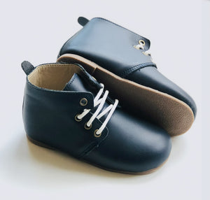 Dark navy leather baby Oxford shoes with white laces, tan soft soles, and rounded toes, displayed on light background.