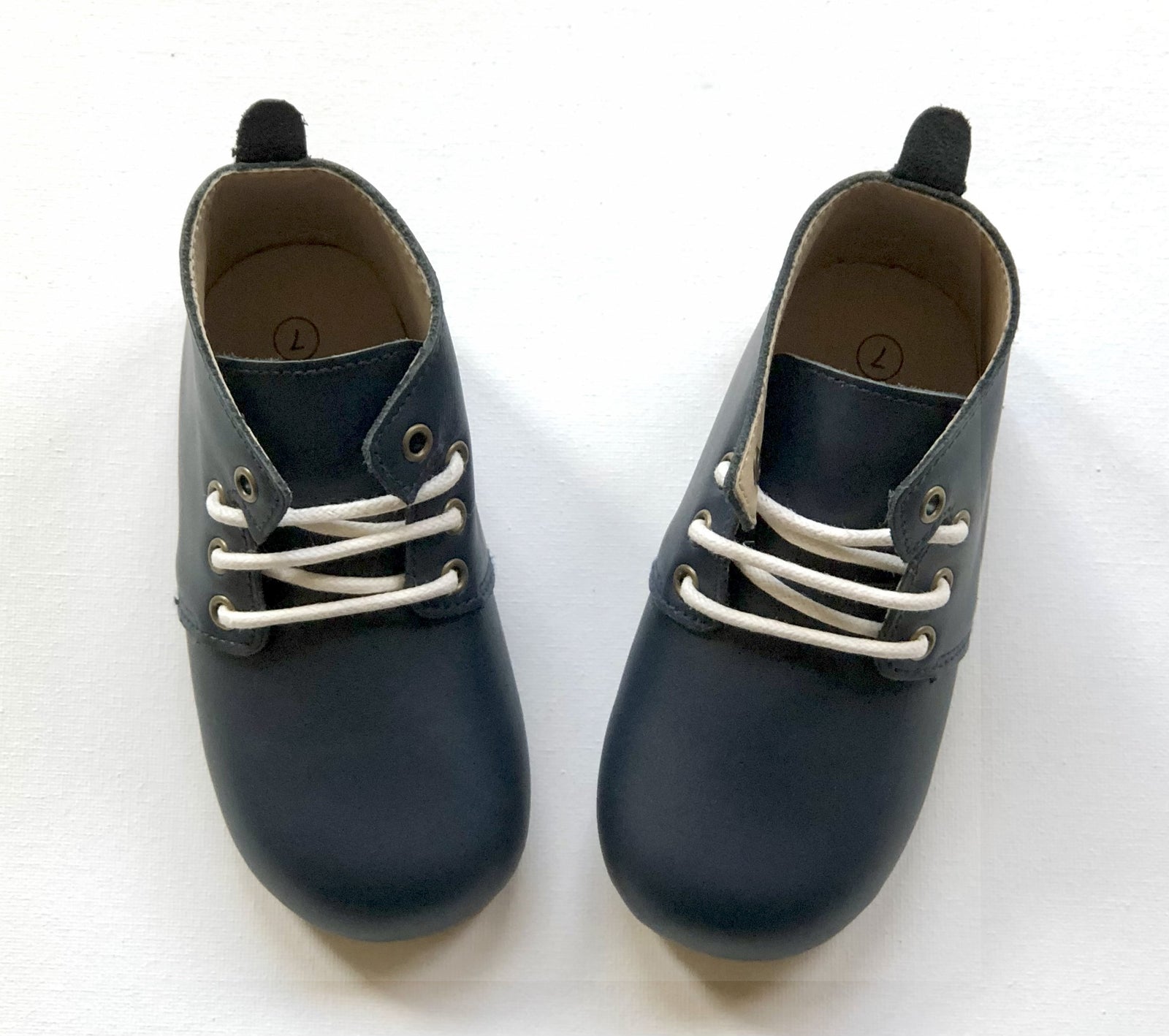 Navy blue leather toddler Oxford shoes with white laces, brown insole, and size “7” marking, positioned side by side on white surface.