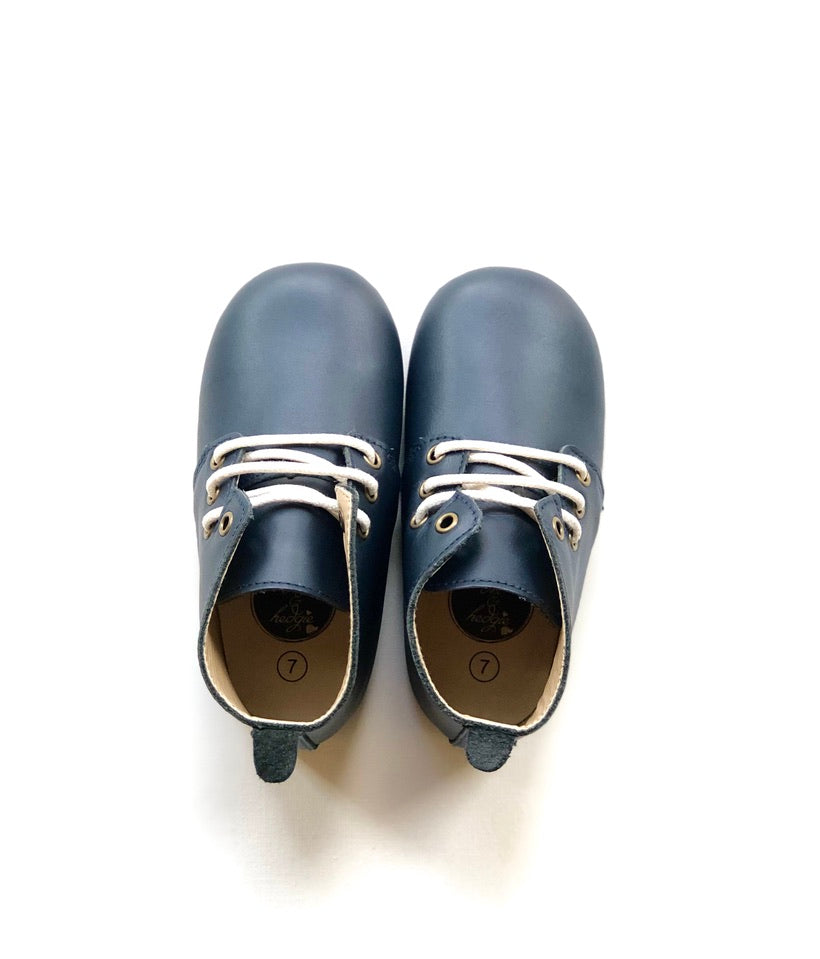 Navy leather baby Oxford shoes with white laces, pull tab at heel, and size “7” insole branding, displayed on white background.