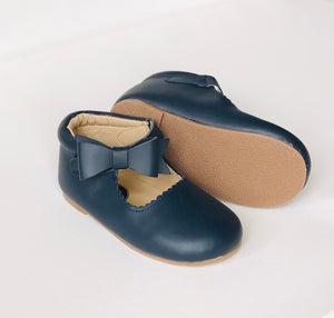 Navy blue baby shoes with scalloped edges, front bow detail, and light brown rubber sole, displayed on white surface.