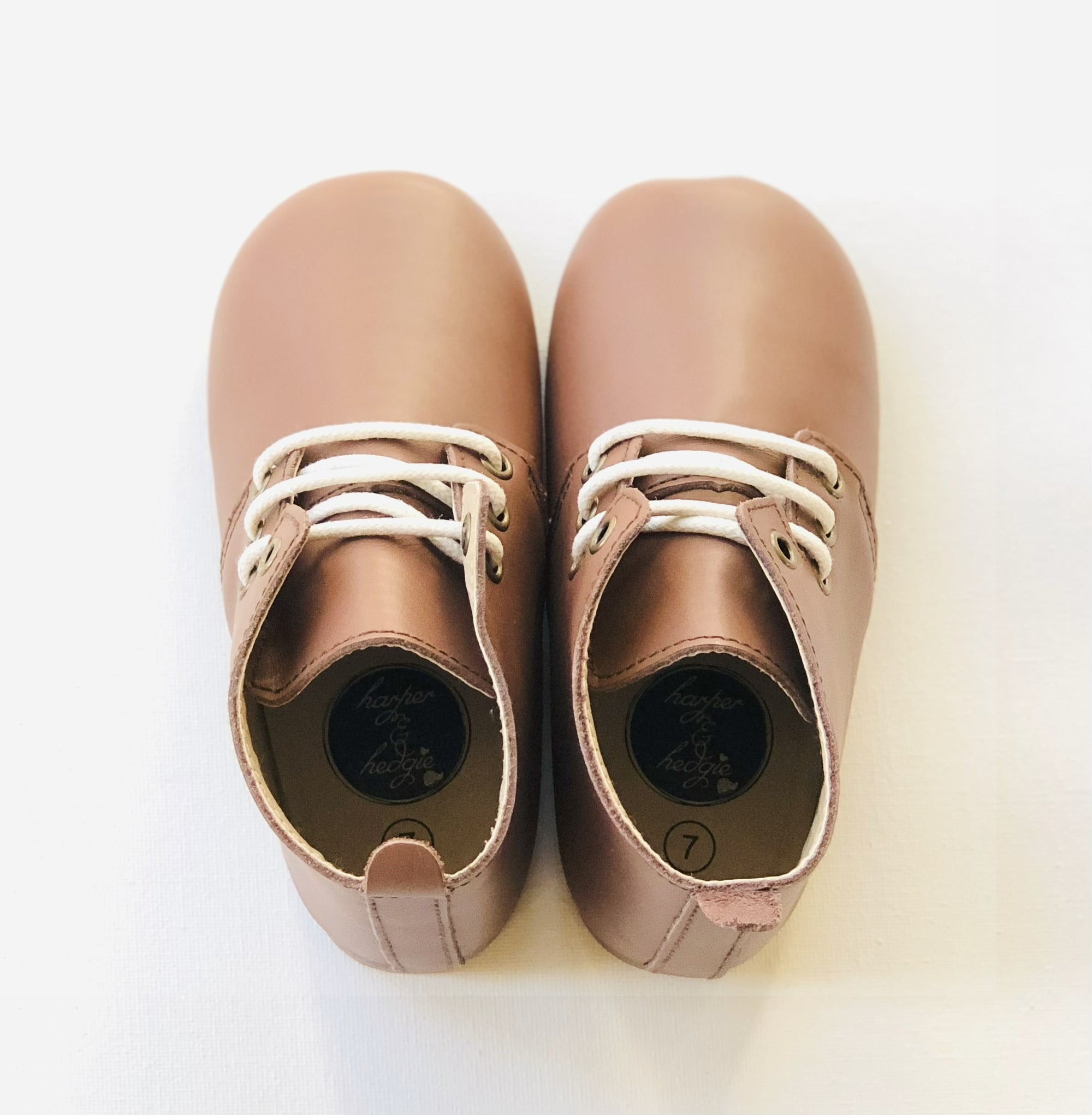 Light brown leather baby shoes with white laces and  displayed side by side on white background.