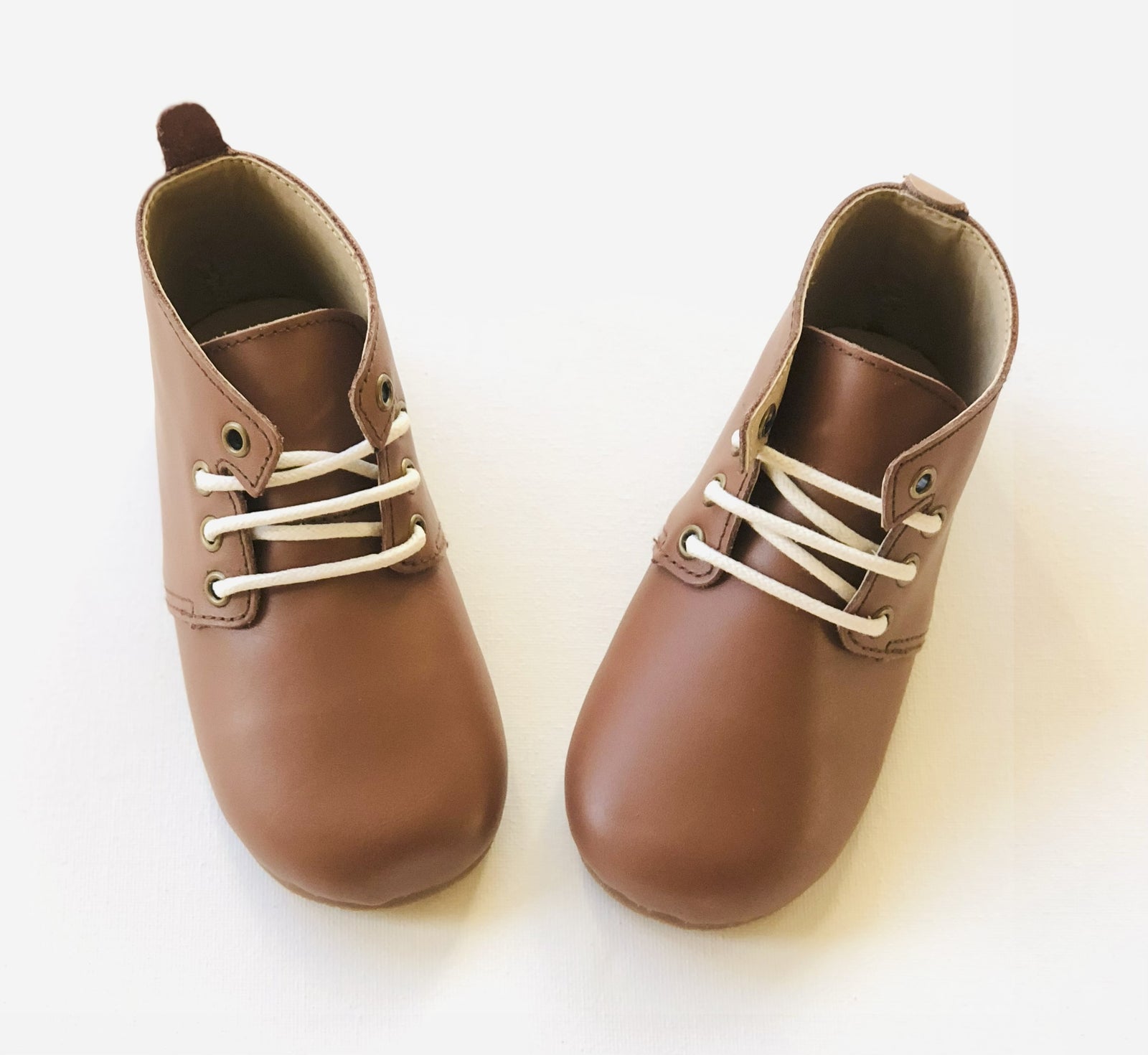 Smooth brown leather baby shoes with white laces and rounded toes, positioned side by side on white background for product clarity.