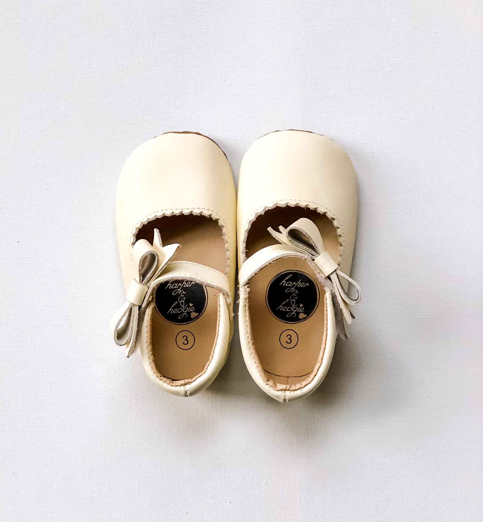 Cream toddler dress shoes with bow detail and strap, size 3 infant footwear on white background.