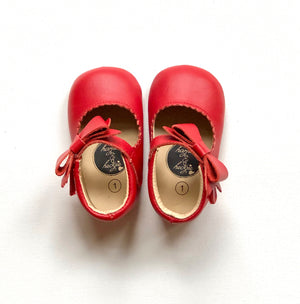Red leather baby Mary Janes with scalloped trim and side bows, featuring Harper & Hedgie branding and size label.