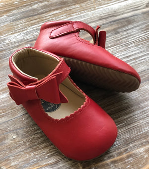 Red baby shoes with zigzag sole and hook-and-loop strap, styled on wooden surface for product detail and texture.