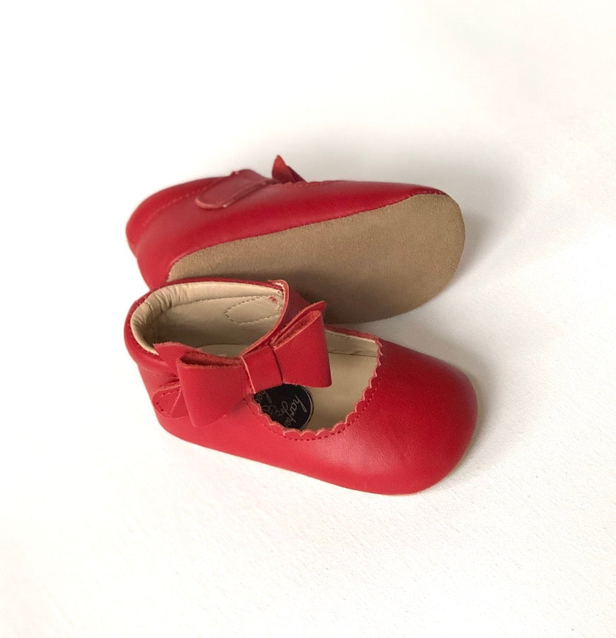 Red Mary Janes with scalloped edges and tan sole, featuring decorative bow and soft soles.