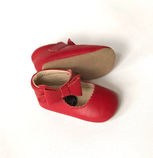 Red Mary Janes with scalloped edges and tan sole, featuring decorative bow and soft soles.