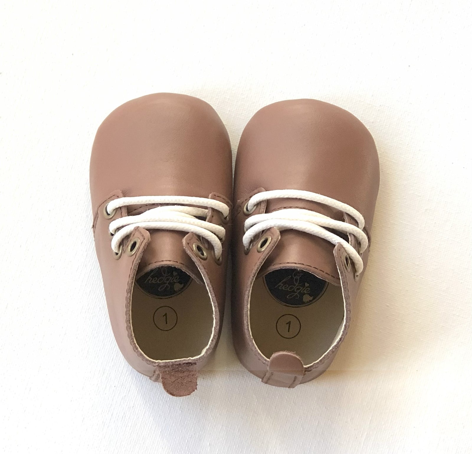 Brown leather baby Oxford shoes with white laces and rounded toes, placed side by side on light background for product clarity.