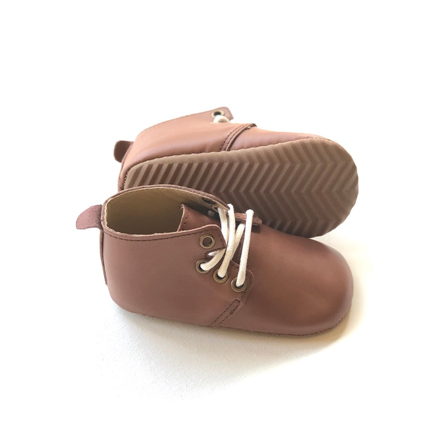 Brown leather infant shoes with white laces, pull tab, and zigzag tread sole, displayed upright and side view on light background.
