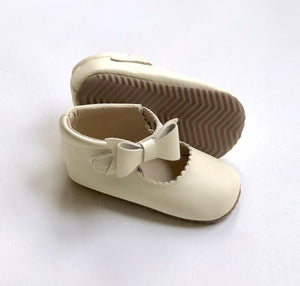 Cream baby Mary Janes with scalloped trim, front bows, and herringbone sole – designed for grip and elegance.