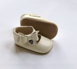 Cream baby shoes with scalloped edges, soft soles, and bow detail – shown upright and side view for product clarity.