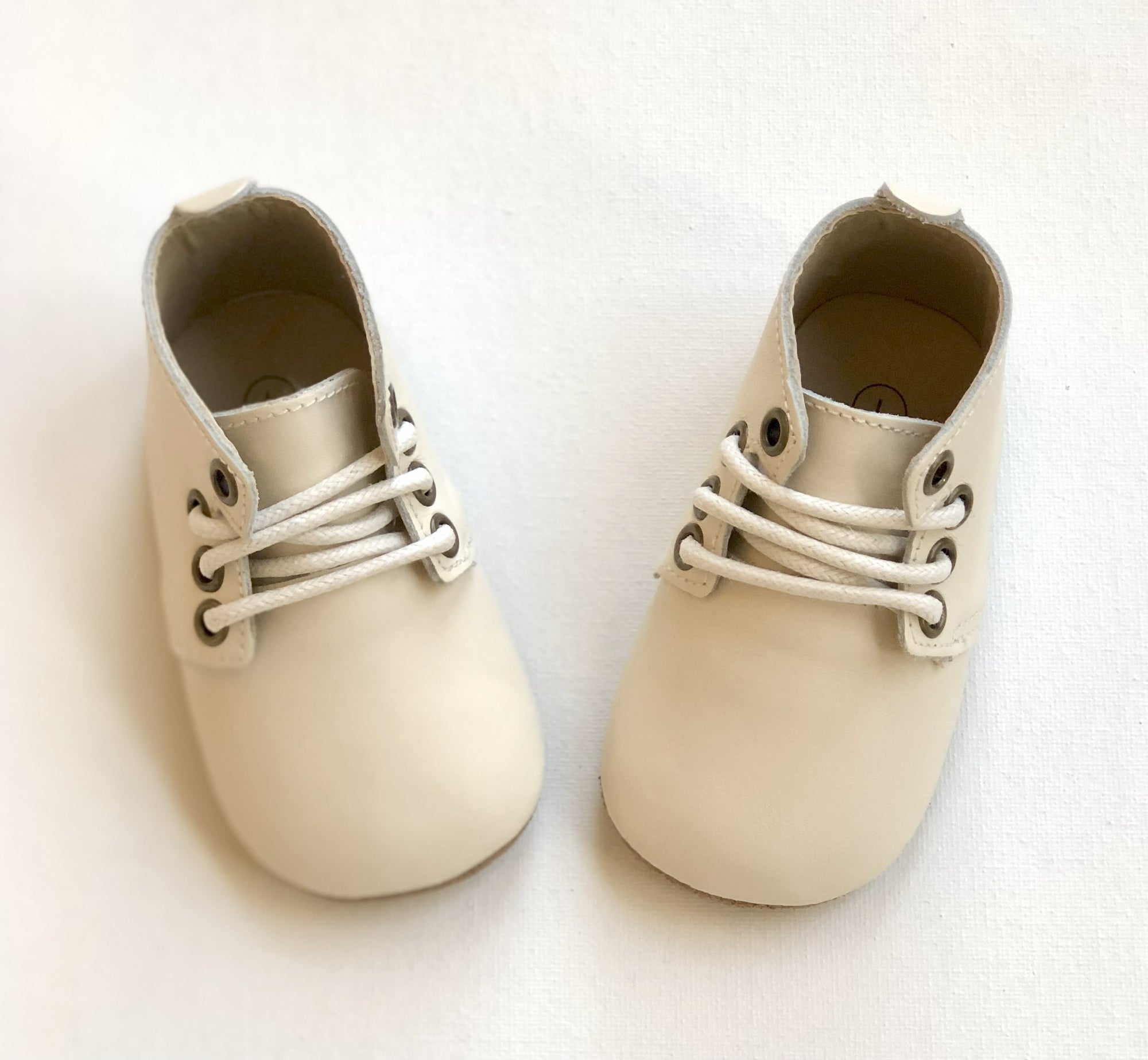Cream leather baby Oxford shoes with white laces and rounded toes, displayed on light background for product clarity.