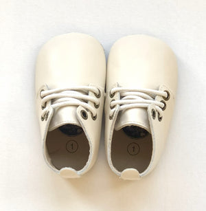 Cream leather baby shoes with white laces and size “1” insole marking, positioned side by side on light surface.