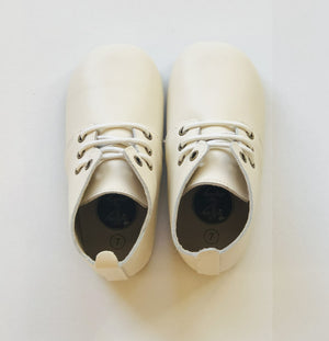 Cream leather baby Oxford shoes with white laces, pull tab, and size “7” insole branding, positioned side by side on white surface.