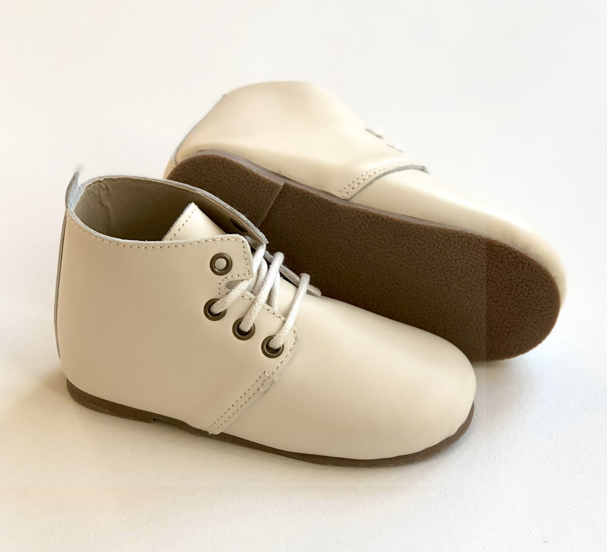 Beige leather baby Oxford shoes with white laces and brown hard soles, one upright and one on its side to show tread detail.