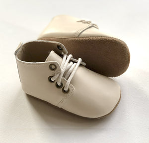 Cream leather baby Oxford shoes with white laces, one upright and one on its side to show soft sole detail.